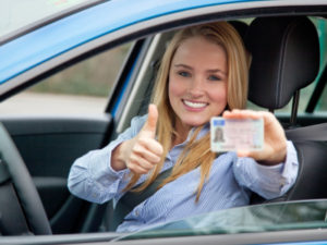 A woman in the drivers seat of her car holding up two thumbs up.