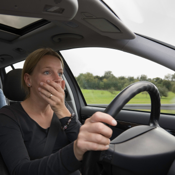 A woman driving in her car with one hand on the steering wheel.