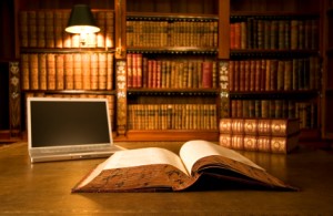 A laptop and open book on the table in front of some books.