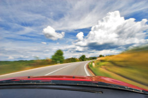 A car driving down the road with clouds in the background.