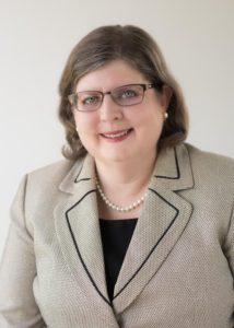 A woman in glasses and a jacket smiles for the camera.