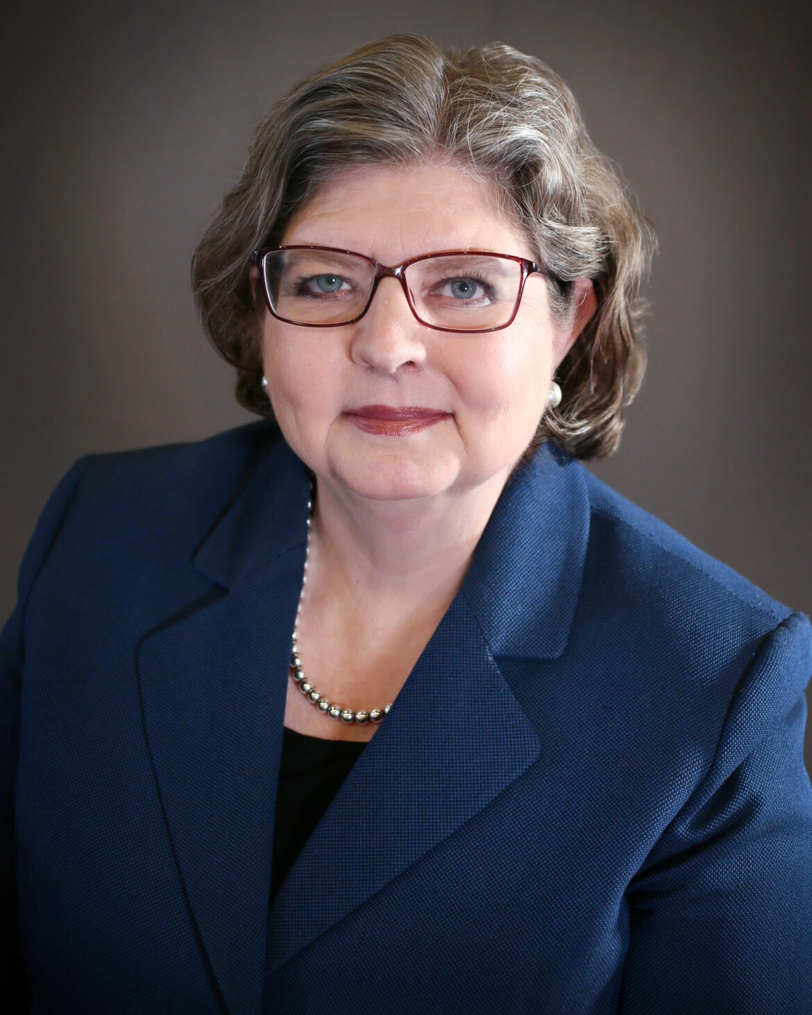 Woman wearing glasses and blue suit jacket.